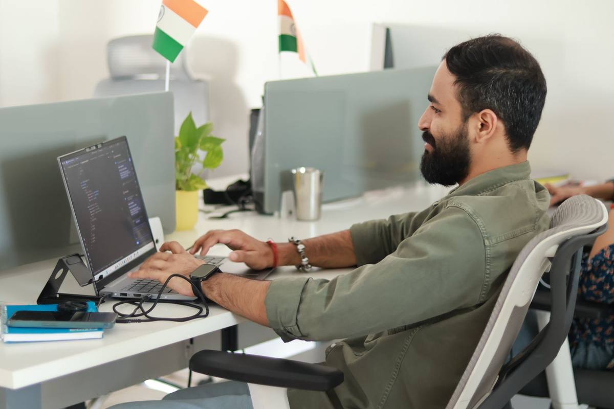 A man working at his computer in an Indian office, with India’s flag on the desk