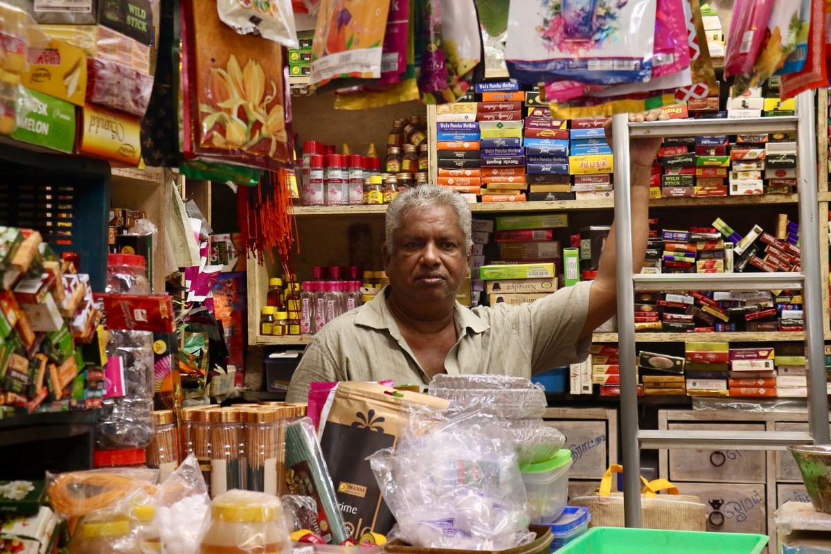 A shopkeeper standing behind the counter of a busy Indian store